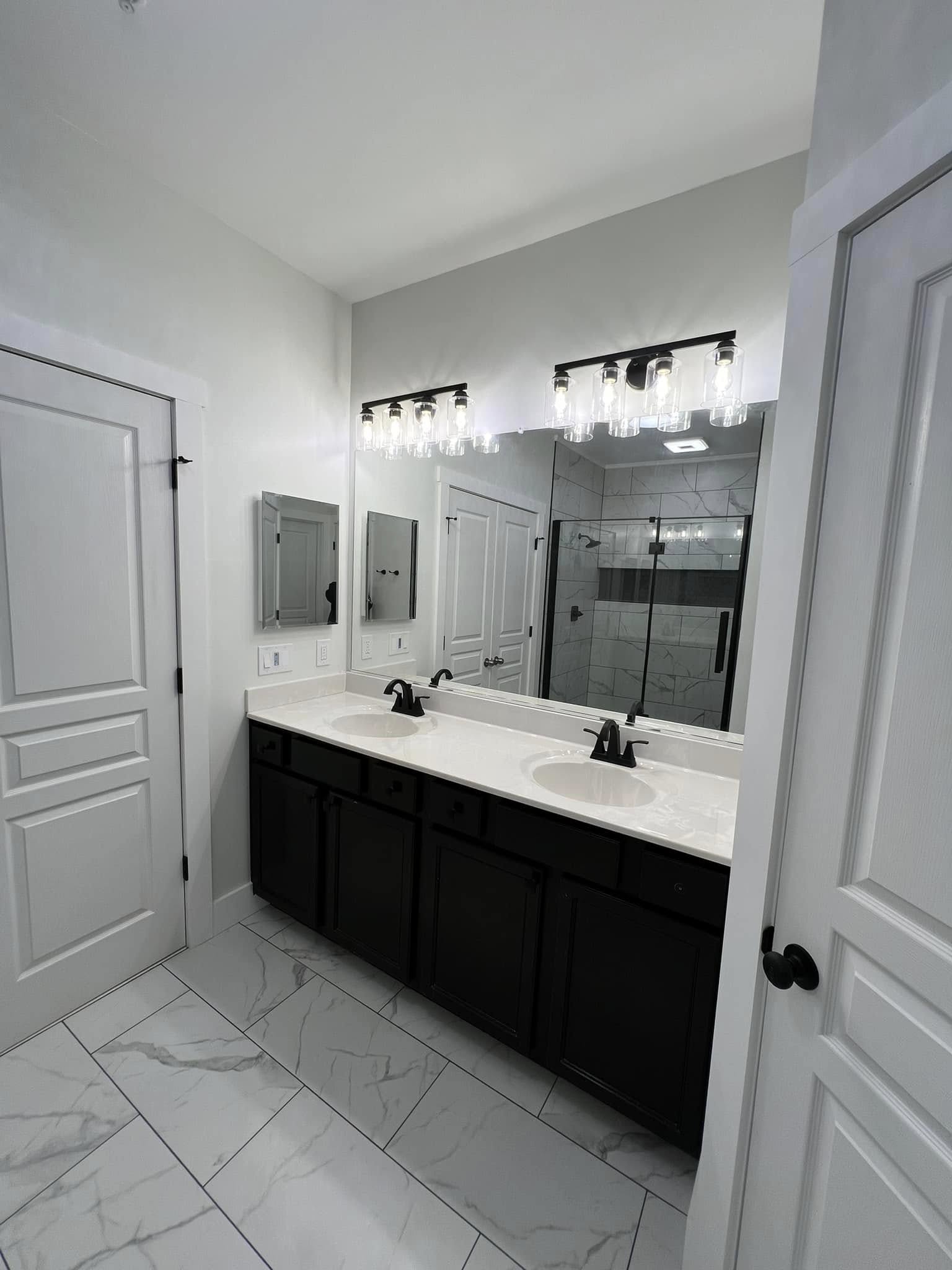 Remodeled bathroom with double vanity, marble-look tile, and matte black fixtures