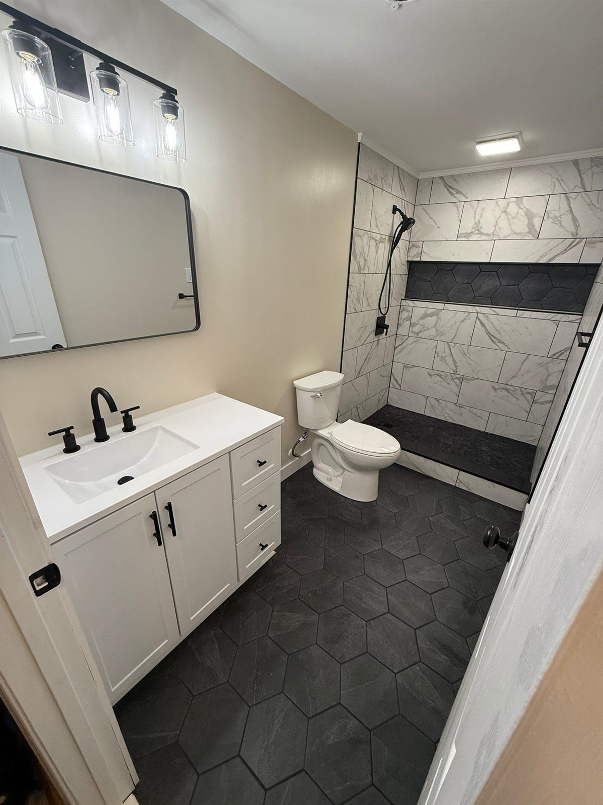 Full bathroom remodel with white vanity, matte black fixtures, and a marble-tile shower