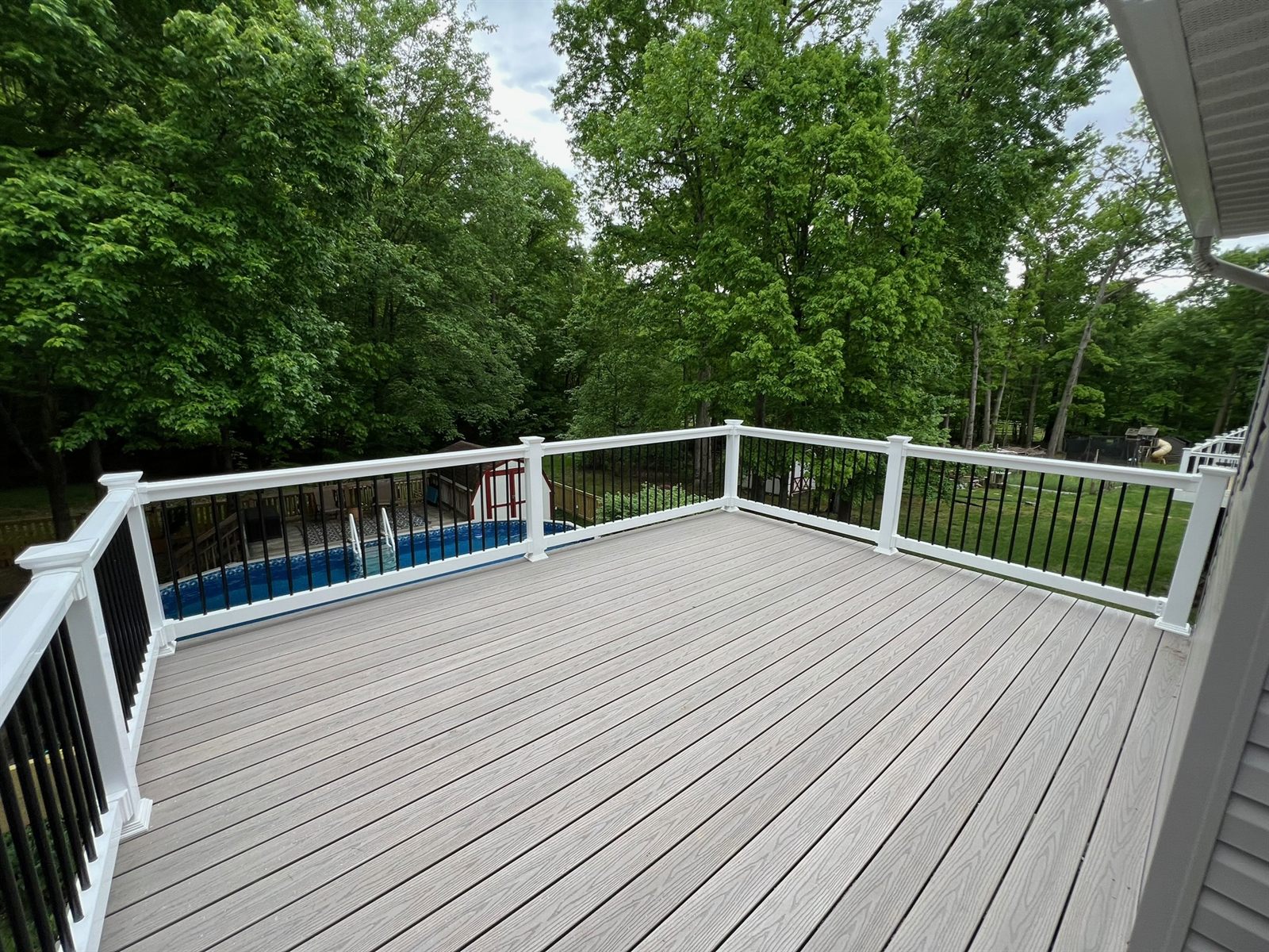 Composite deck overlooking an in-ground pool and wooded backyard