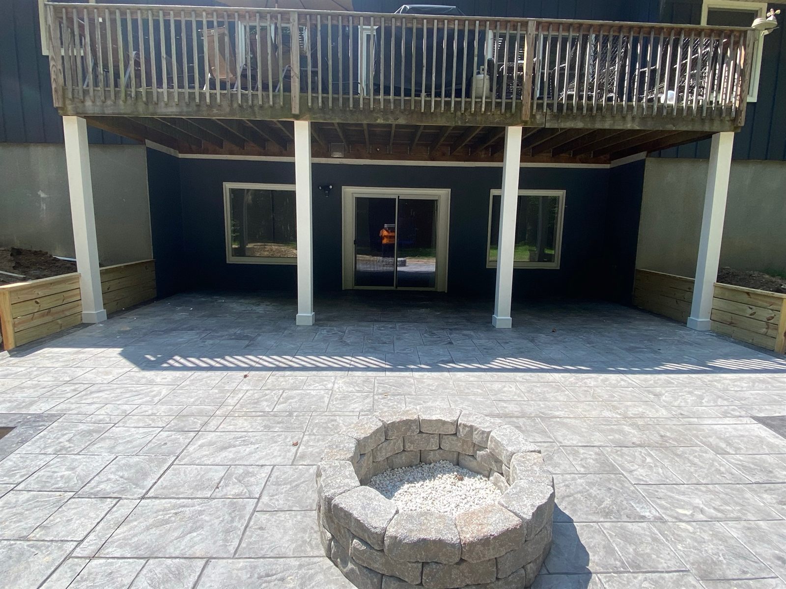 Stamped-concrete patio with a stone fire pit beneath an elevated deck